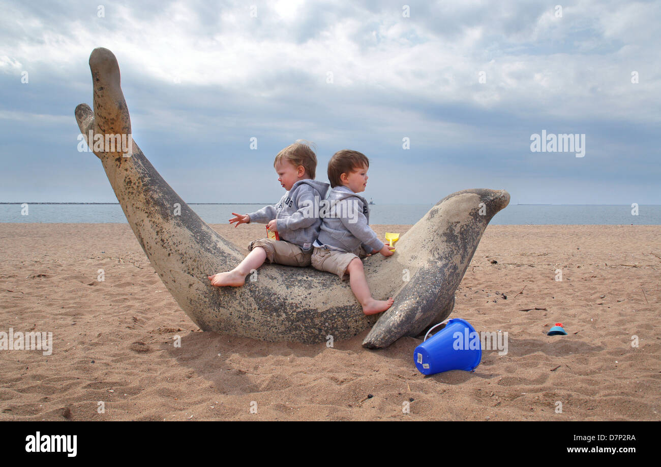 Twin brothers play on a cement sculpture of a seal at the beach in New Haven CT USA Stock Photo