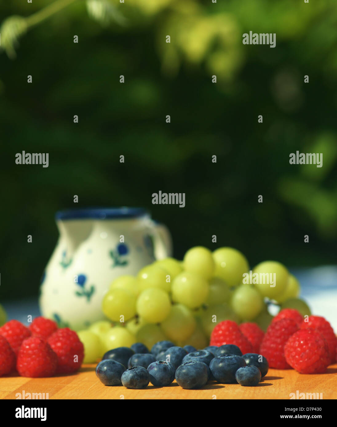 Fresh blueberries, raspberries and grapes on a garden table. Focus on blueberries Stock Photo