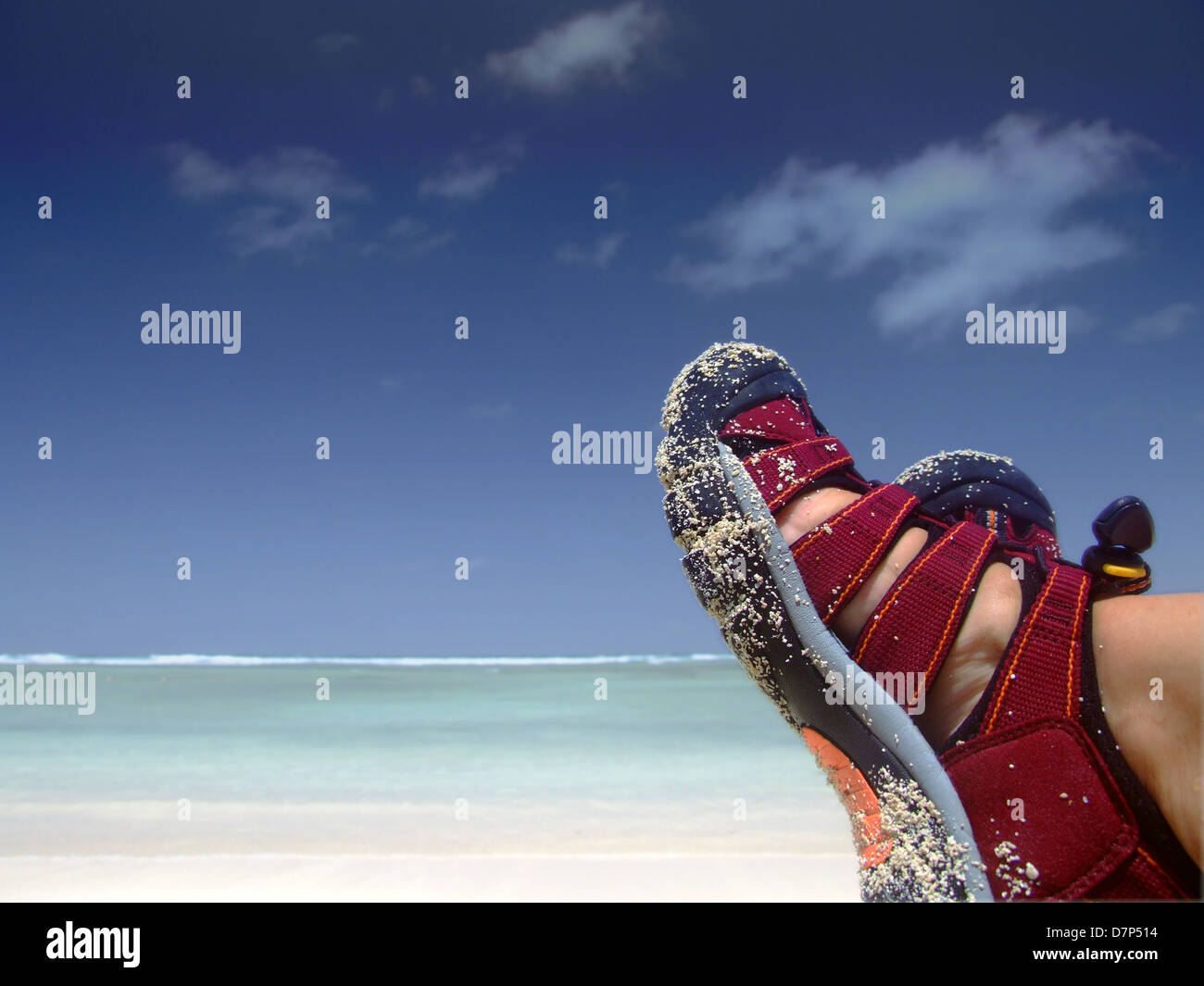 Person wearing red sandals taking rest on the tropical beach. Feet visible only. Stock Photo