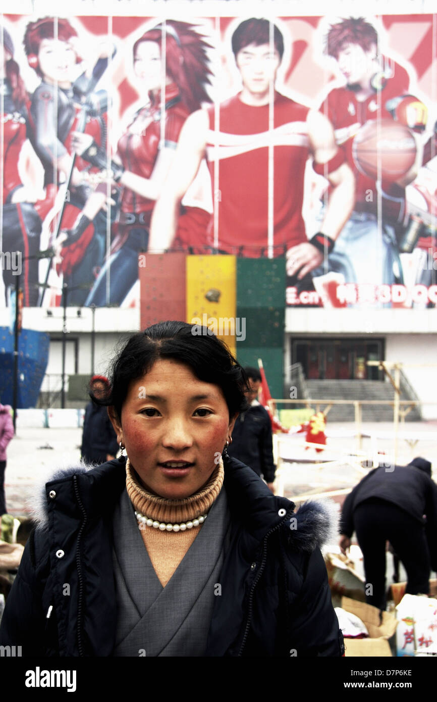 Portrait of young Tibetan woman by huge publicity billboard in a Chengdu market, Sichuan, China. Stock Photo