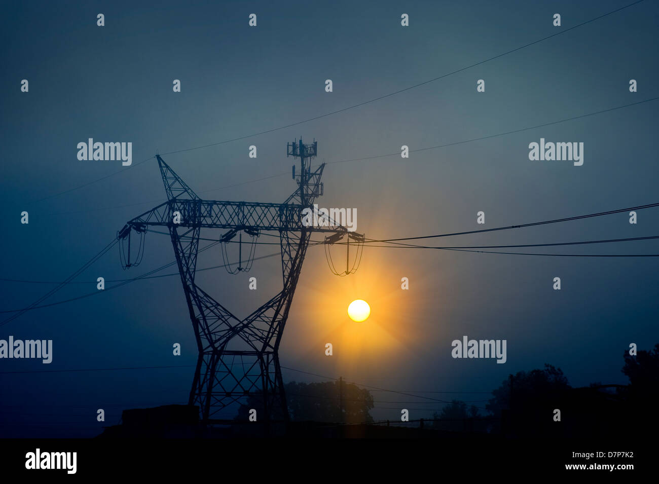 Transmission Tower & Power Lines With Sun Through Fog Stock Photo