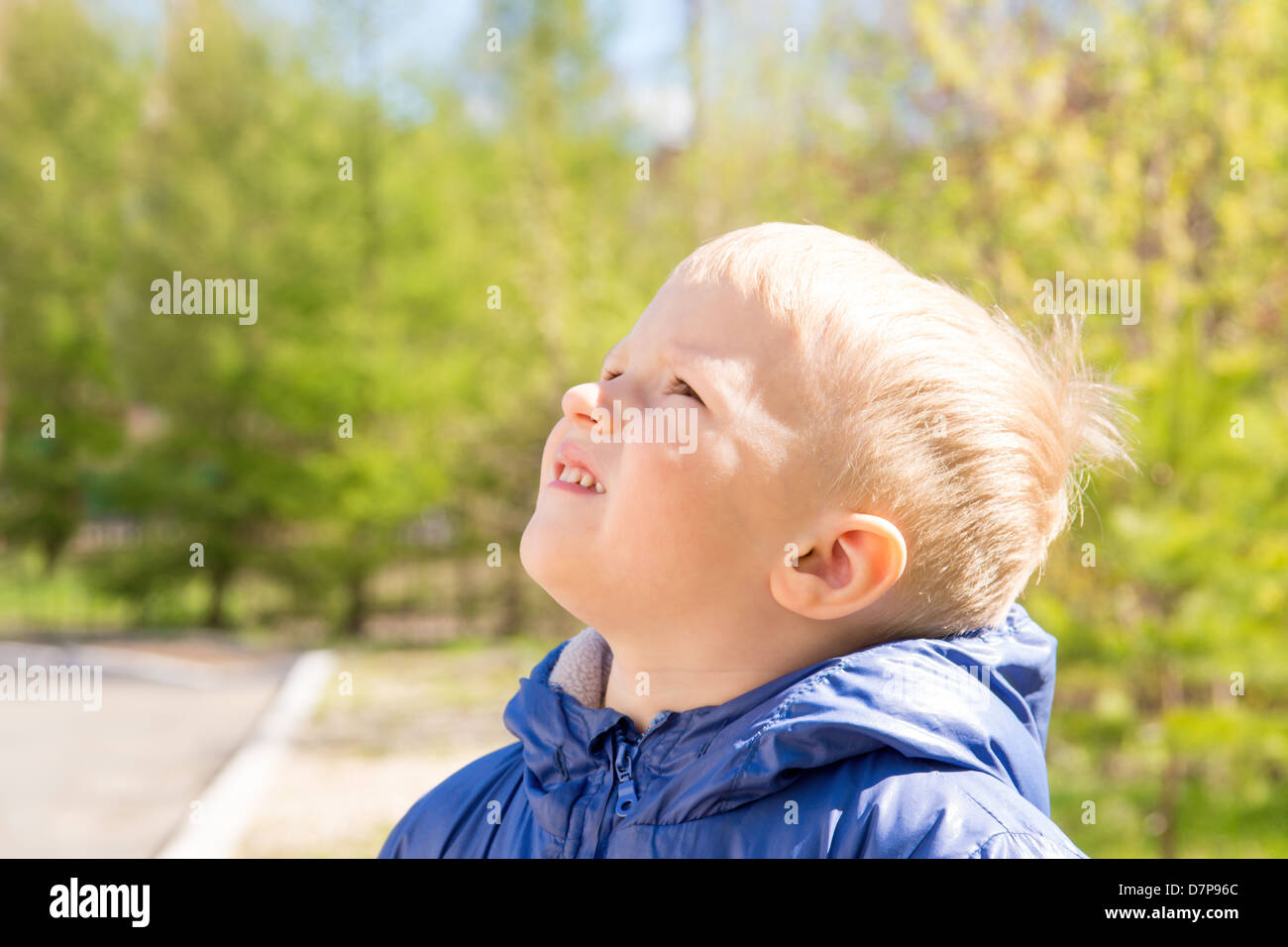 Happy smiling joyful beautiful child (little boy) outdoor in spring green park (garden) looking up. Sunny close up portrait. Stock Photo