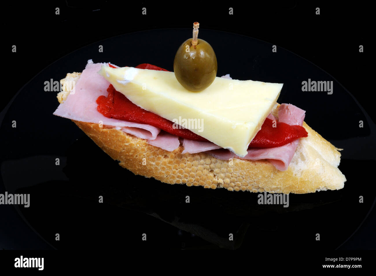 Ham, red pepper and cheese tapa topped with a green olive and served on ...