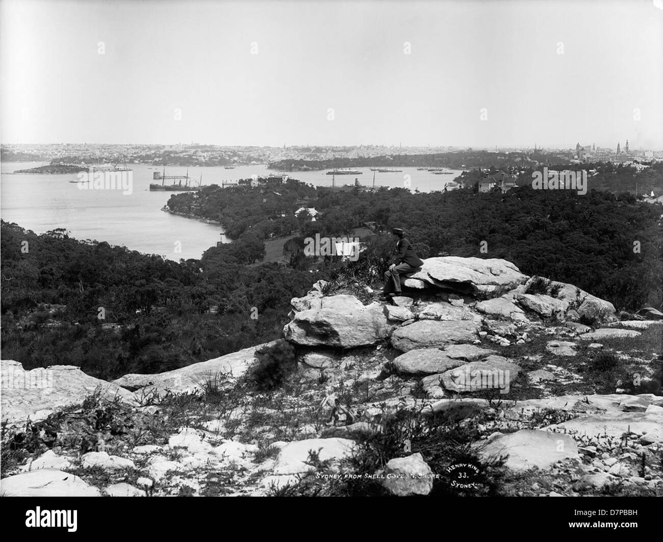 An early 20th-century image of Sydney from Shell Cove, featuring Fort Denison, Garden Island, and the Sydney Harbour skyline. The artwork captures iconic landmarks such as Henry King’s ship, with a view from the North Shore. Stock Photo