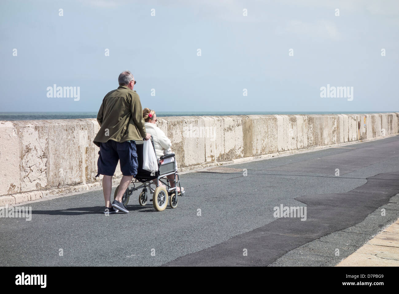 Husband pushing wife in wheelchair at the seaside. Stock Photo