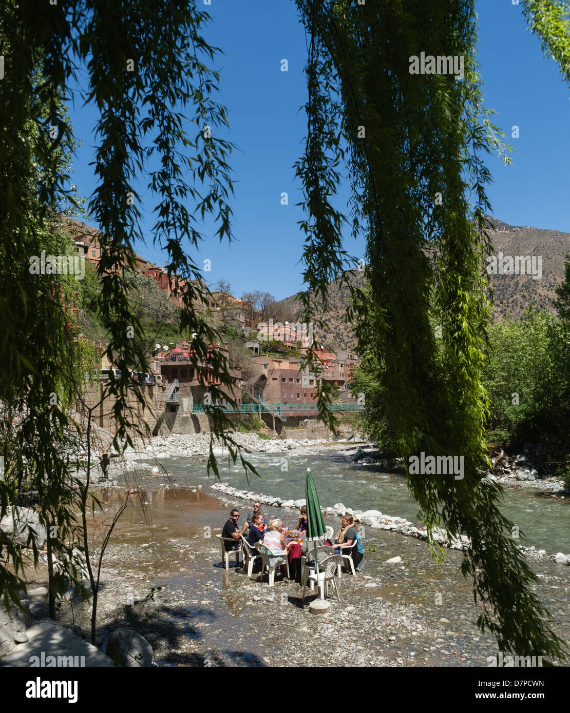 Morocco, Marrakesh - Sti Fatma, Ourika Valley - family dining at a table set right next to the river. Stock Photo