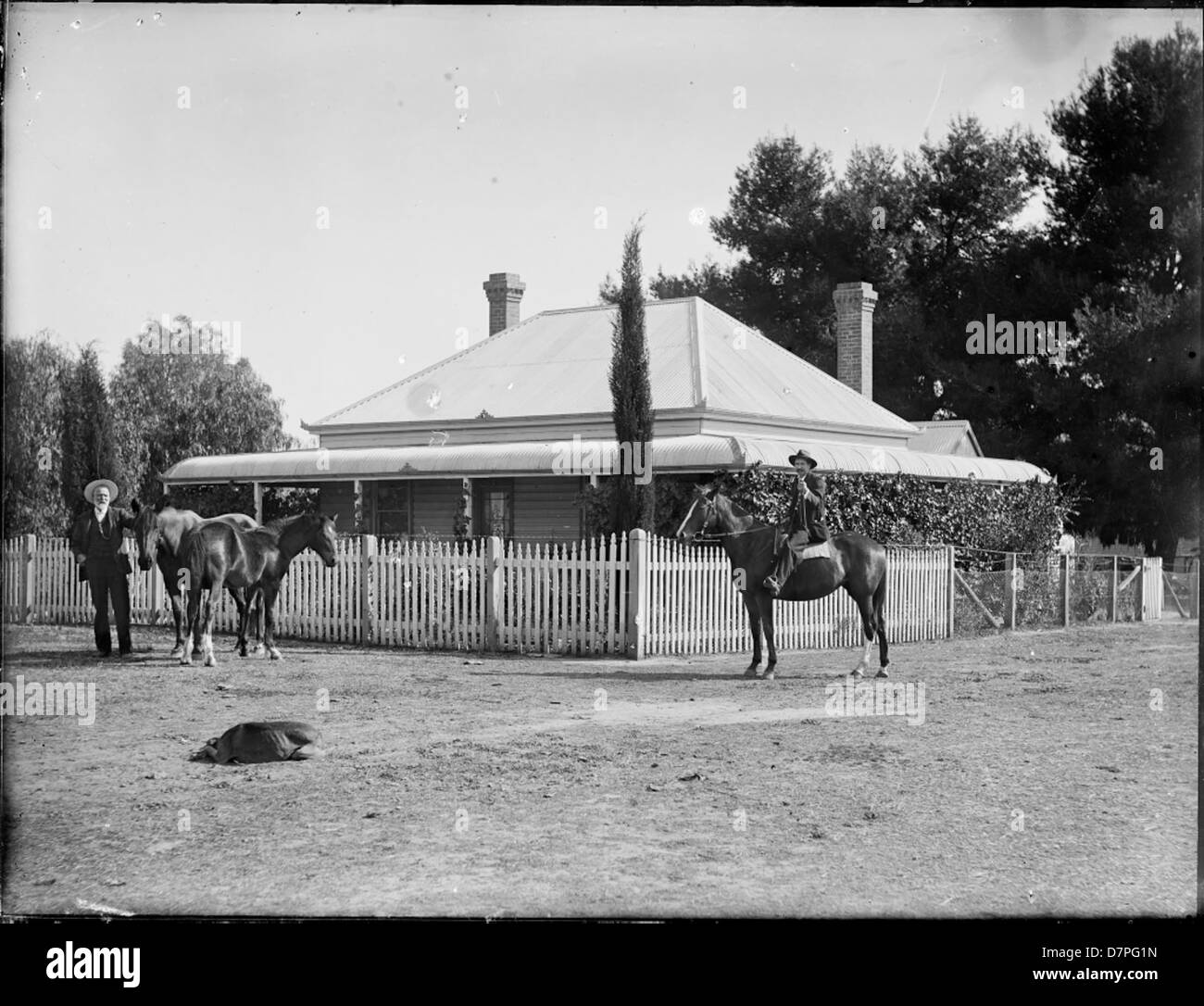 This image shows a colonial-era weatherboard cottage with men and ...