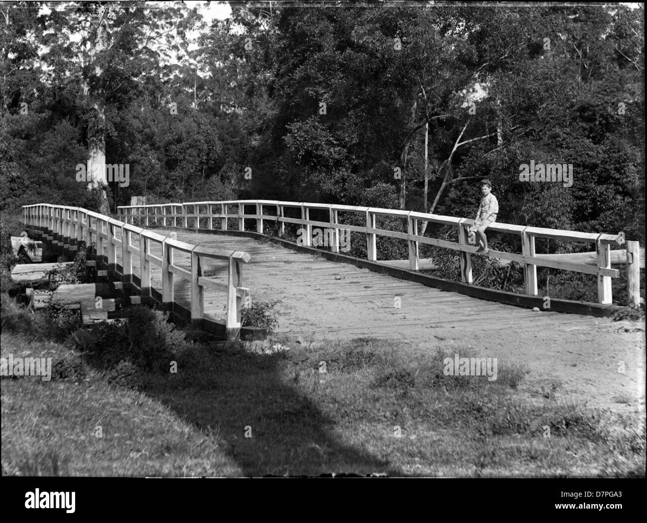 View of wooden bridge with small boy seated on fence Stock Photo