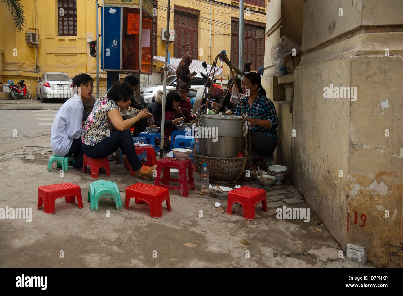 Horizontal view of a street stall selling traditional Pho, noodles, to people happy to sit on a plastic stool on the pavement. Stock Photo