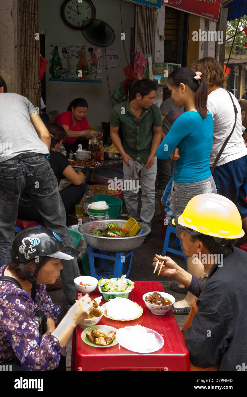 Vertical view of Vietnamese people eating traditional Pho, noodles, at plastic tables on the pavement in Hanoi. Stock Photo