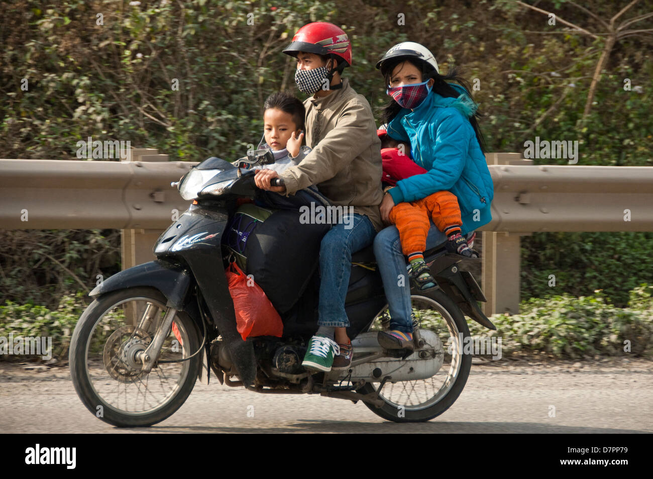 Horizontal portrait of a family of four with suitcases and bags on a moped going home for Tet, Vietnamese New Year. Stock Photo