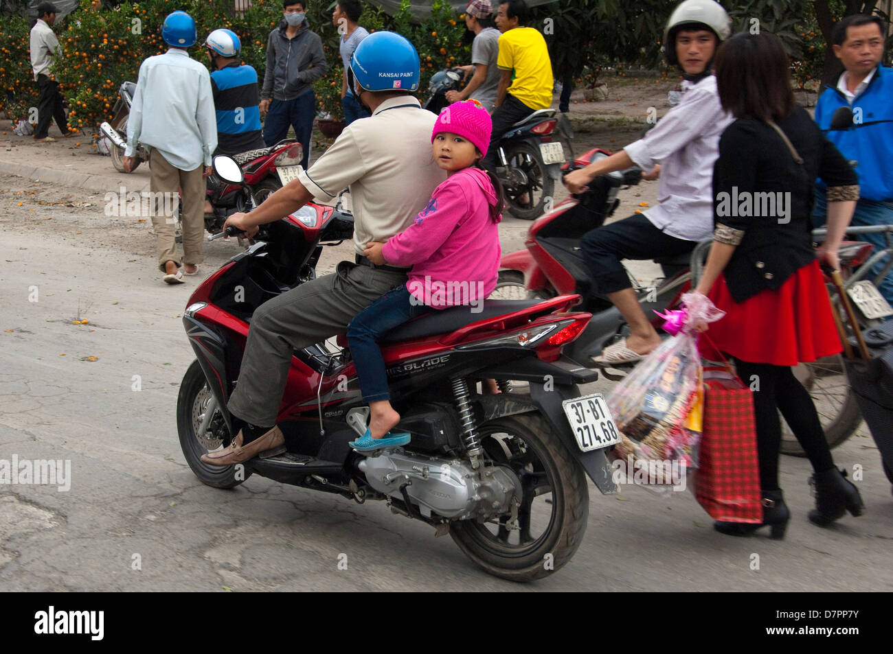 Horizontal portrait of a Dad and his daughter driving down the road on a moped in Hanoi. Stock Photo