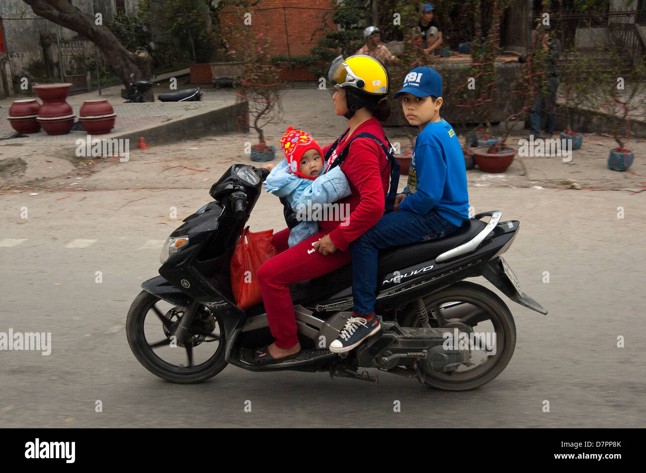 Horizontal portrait of a woman riding a moped with her baby in a harness and her son riding pillion in Hanoi. Stock Photo