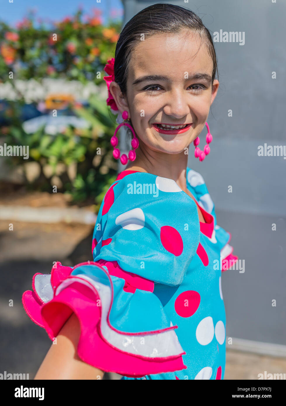 A Hispanic child dancer in her early teens poses in her colorful traditional Flamenco dance outfit, dress, earrings & hair bow. Stock Photo