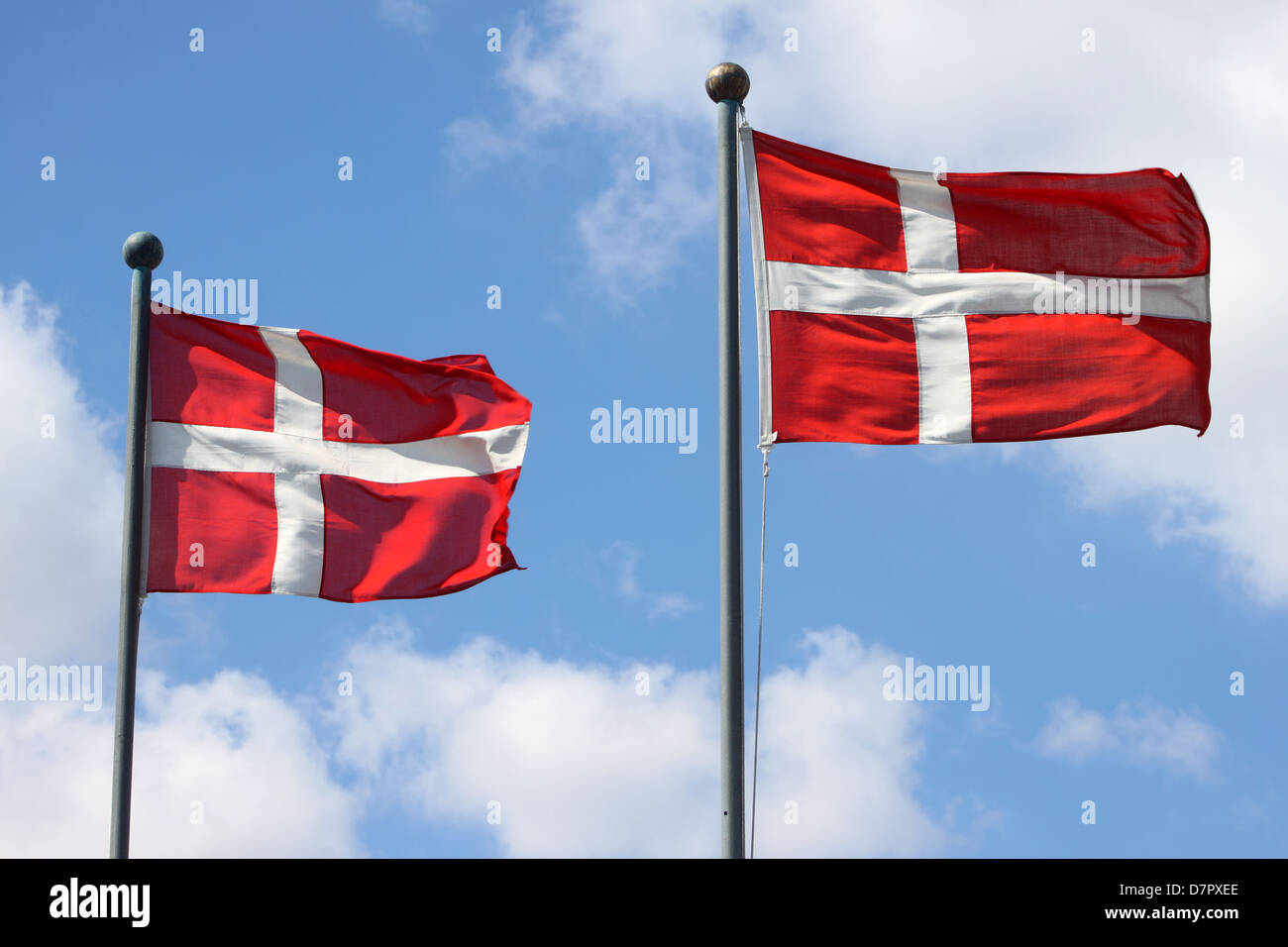 Two Denmark flags waving on wind against the blue sky with clouds Stock Photo