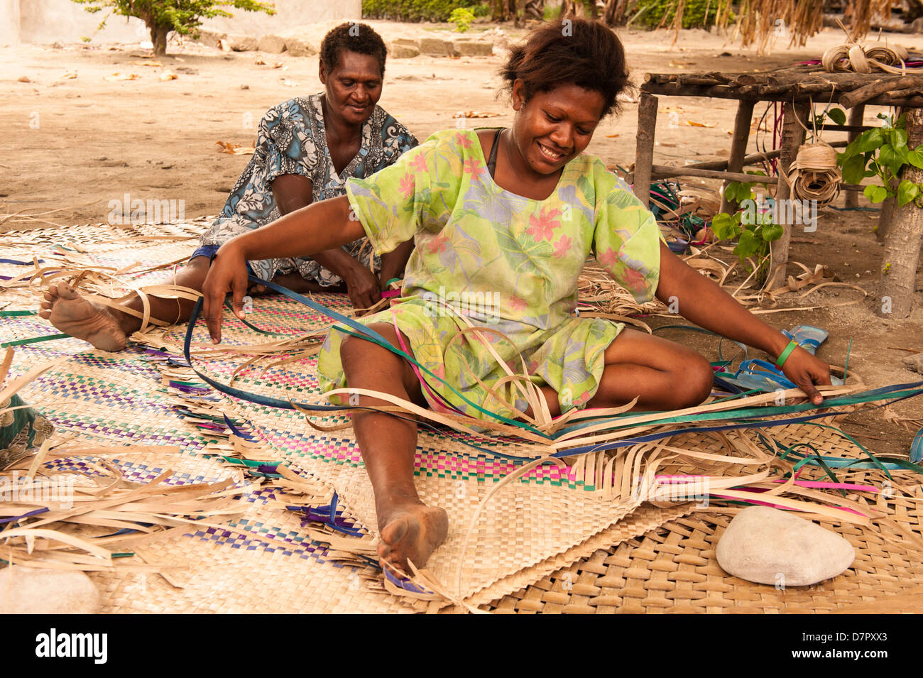 Traditional village life, two women in colourful dresses weaving mats for guests to a large church meeting in their village. Vanuatu Stock Photo