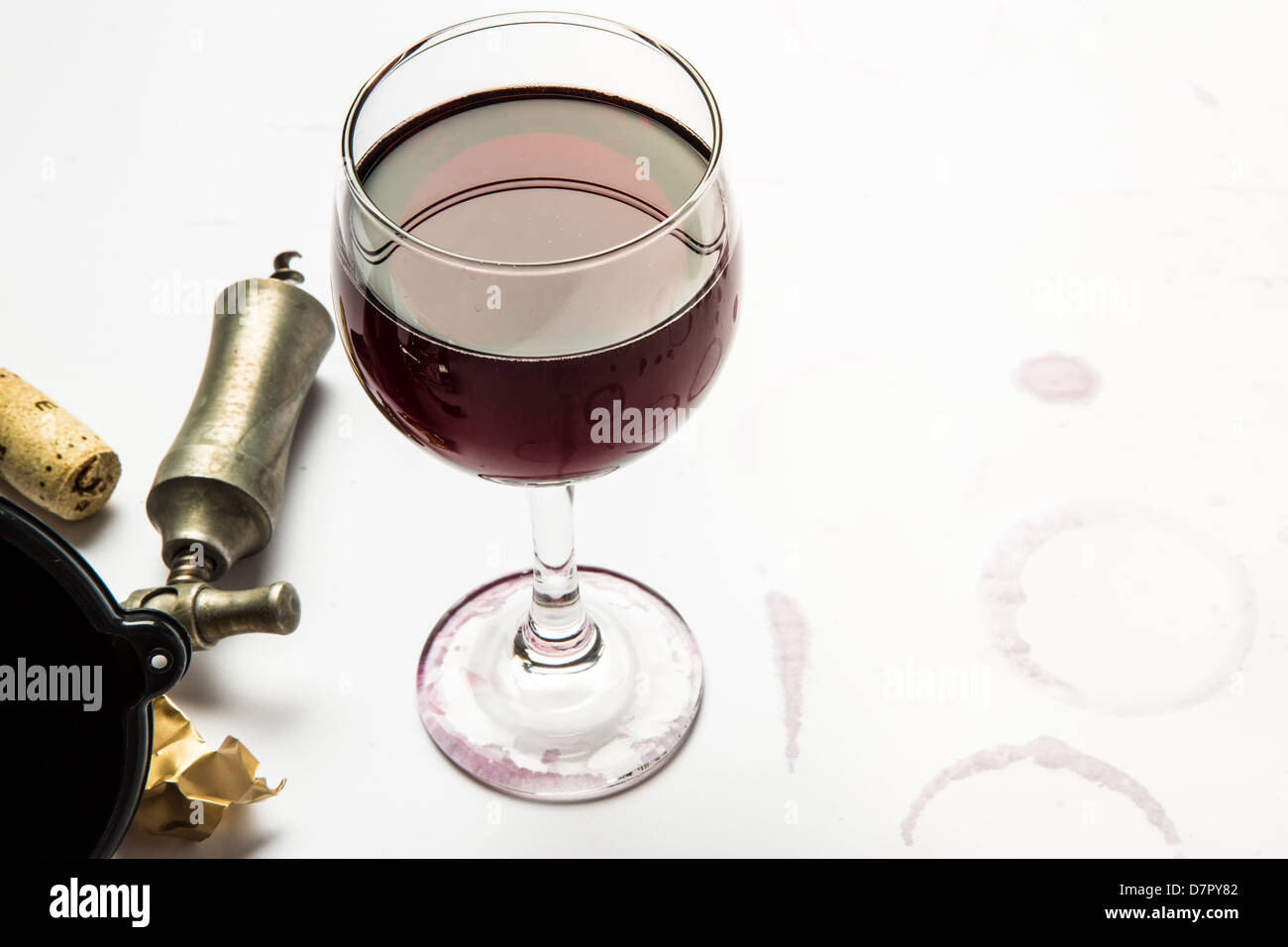 A full glass of red wine with wrapper, cork, and cork screw with wine ring stains from the glass. Stock Photo