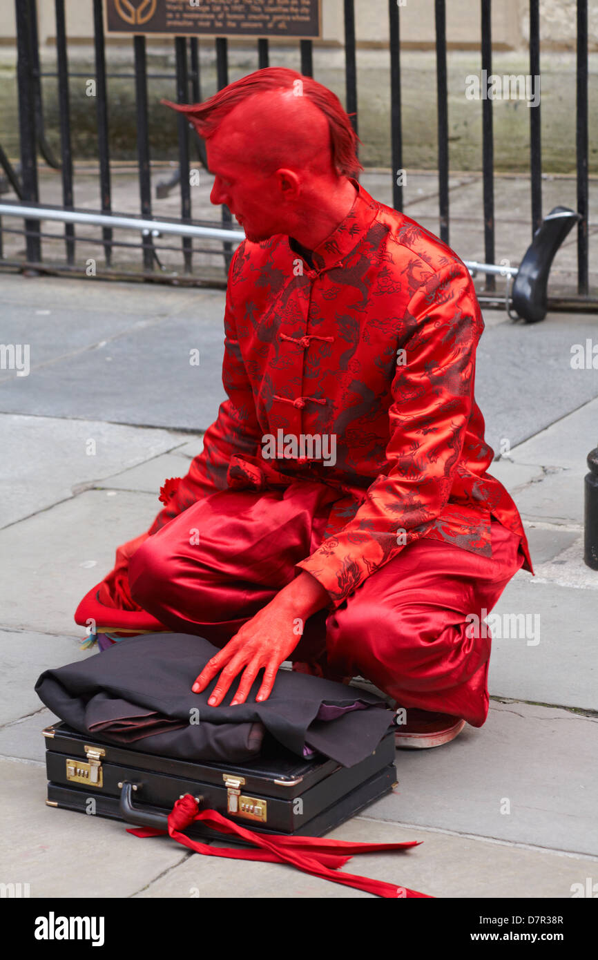 Street performer dressed in red with red face getting ready at Bath, Somerset UK in April Stock Photo