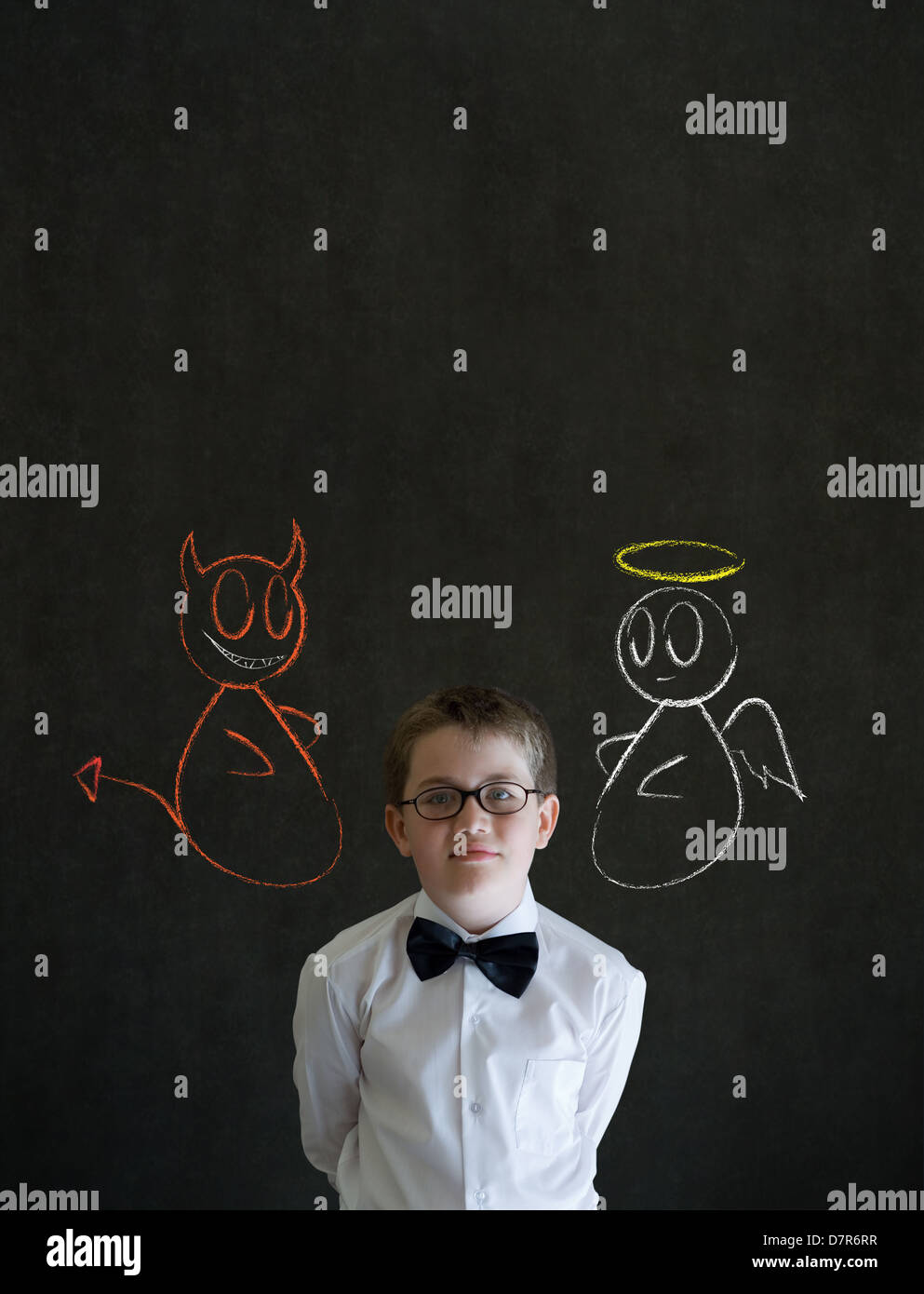 Thinking boy dressed up as business man with chalk angel and devil on shoulder making decision on blackboard background Stock Photo