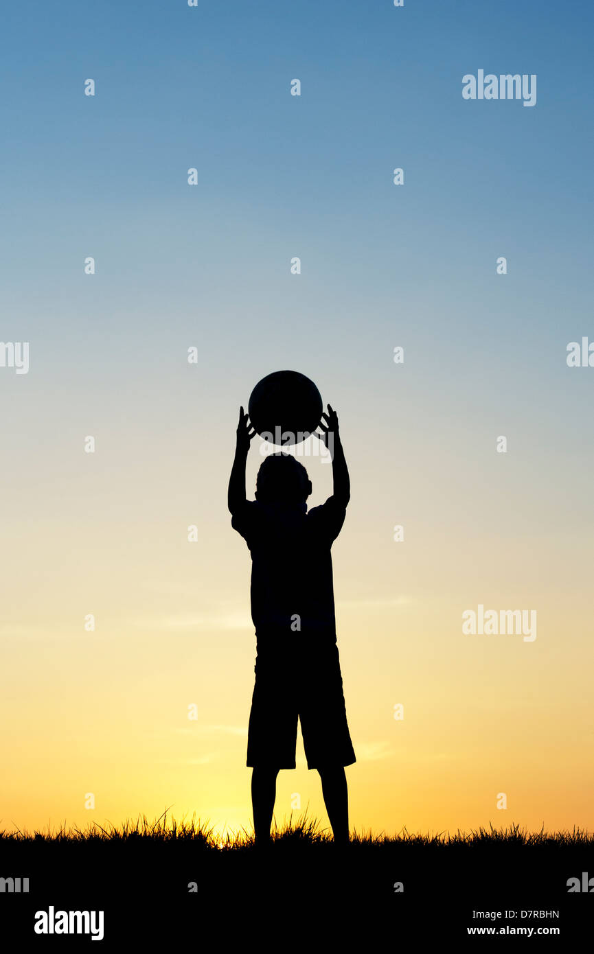 Boy playing with a football at sunset. Silhouette Stock Photo