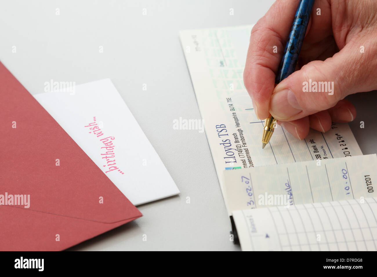 Senior female pensioner writing a Lloyds TSB cheque as a gift to put in a birthday greetings card. England, UK, Britain. Stock Photo