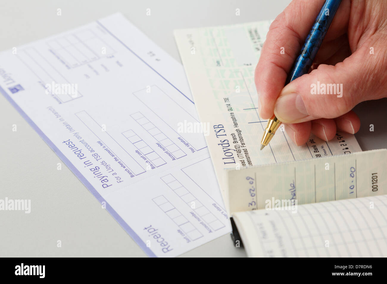 Woman pensioner saving money writing a Lloyds joint account cheque to pay in to a bank on a paying in credit slip. England UK Britain Stock Photo