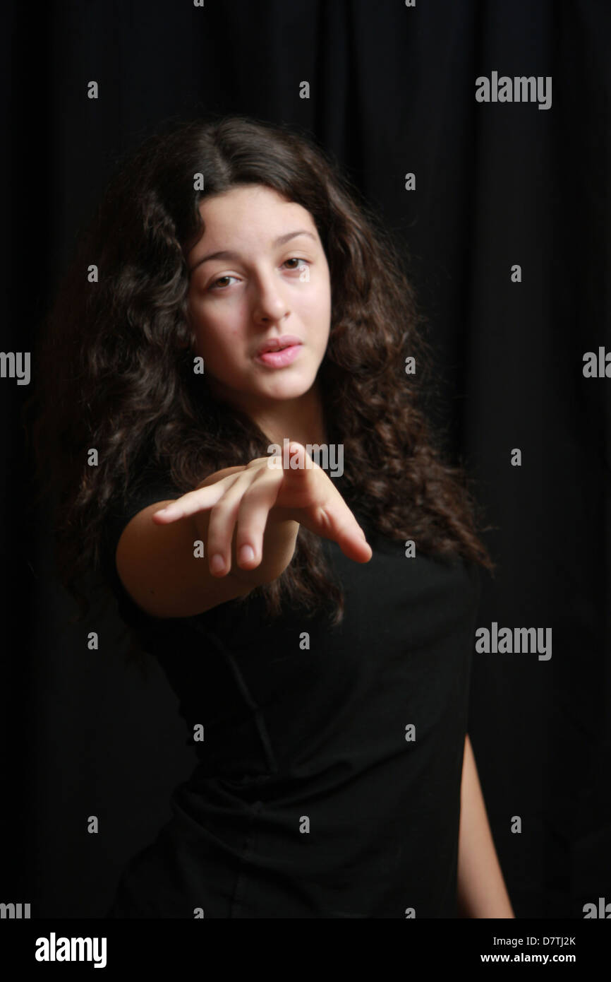 teen girl pointing out with curly dark hair no make up dressed in black head to waist shot Stock Photo