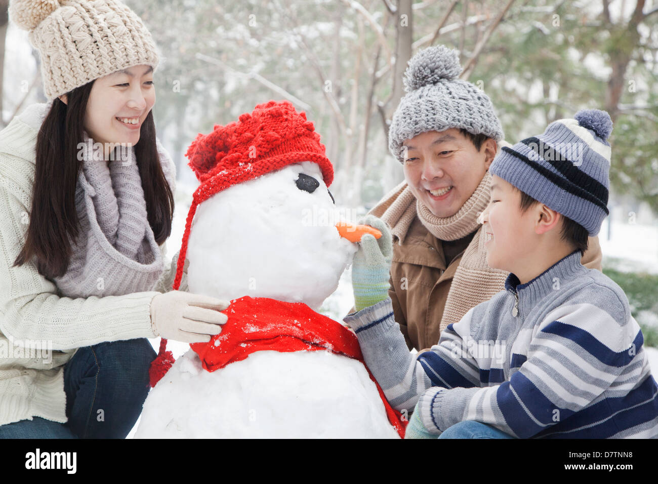 Family making snowman in a park in winter Stock Photo. 