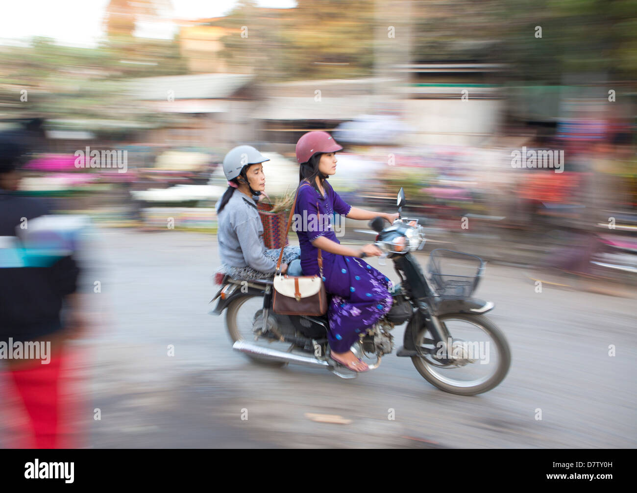 Panned and blurred shot, creating a sense of movement, of two women riding moped through a market, Mandalay, Burma Stock Photo
