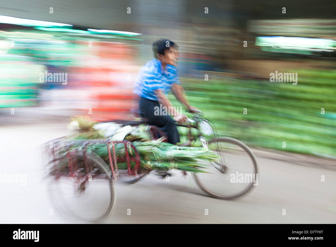 Panned and blurred image to add a sense of movement of a man cycling through Thiri Mingalar market, Yangon (Rangoon), Burma Stock Photo