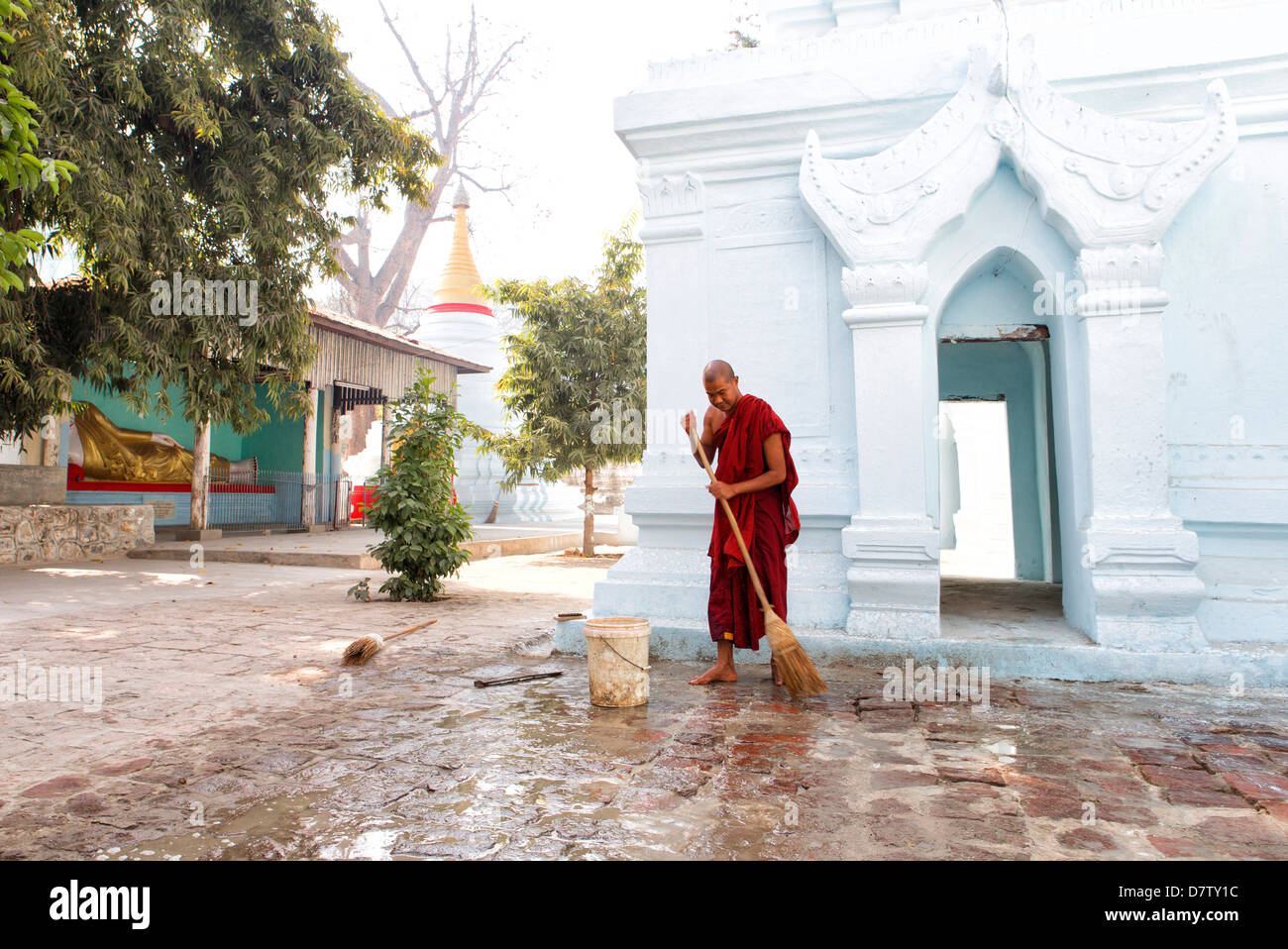Buddhist monk cleaning paving outside a small temple near the famous U Bein teak bridge, Amarapura, near Mandalay, Burma Stock Photo