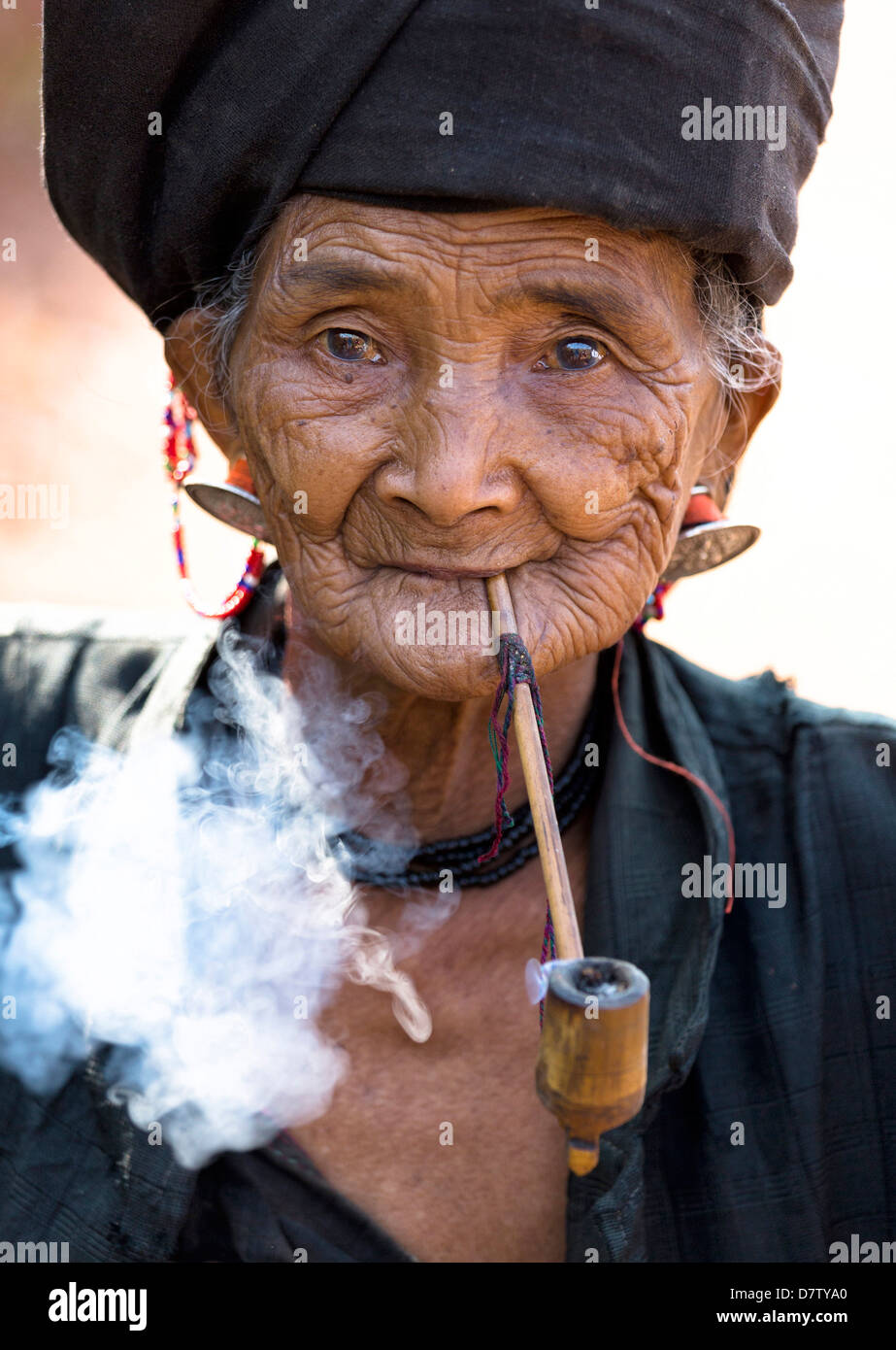 Woman of the Ann tribe in traditional black dress smoking a pipe outside a hill village near Kengtung, Shan State, Burma Stock Photo