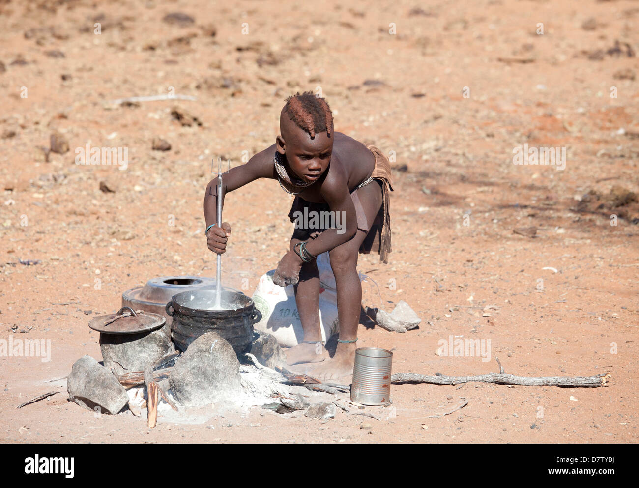 Young Himba boy cooking food on open fire in his village, Kunene Region (formerly Kaokoland) in the far north of Namibia Stock Photo