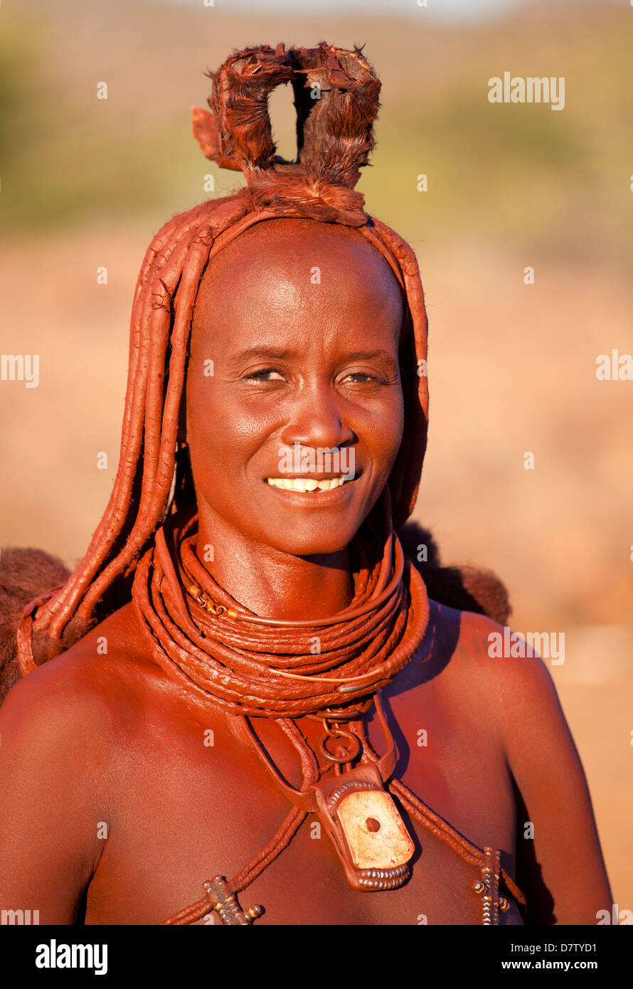 Himba woman inside a mud dwelling hut wearing dress and jewellery and covered in Otjize, Kunene Region, Kaokoland, Namibia Stock Photo