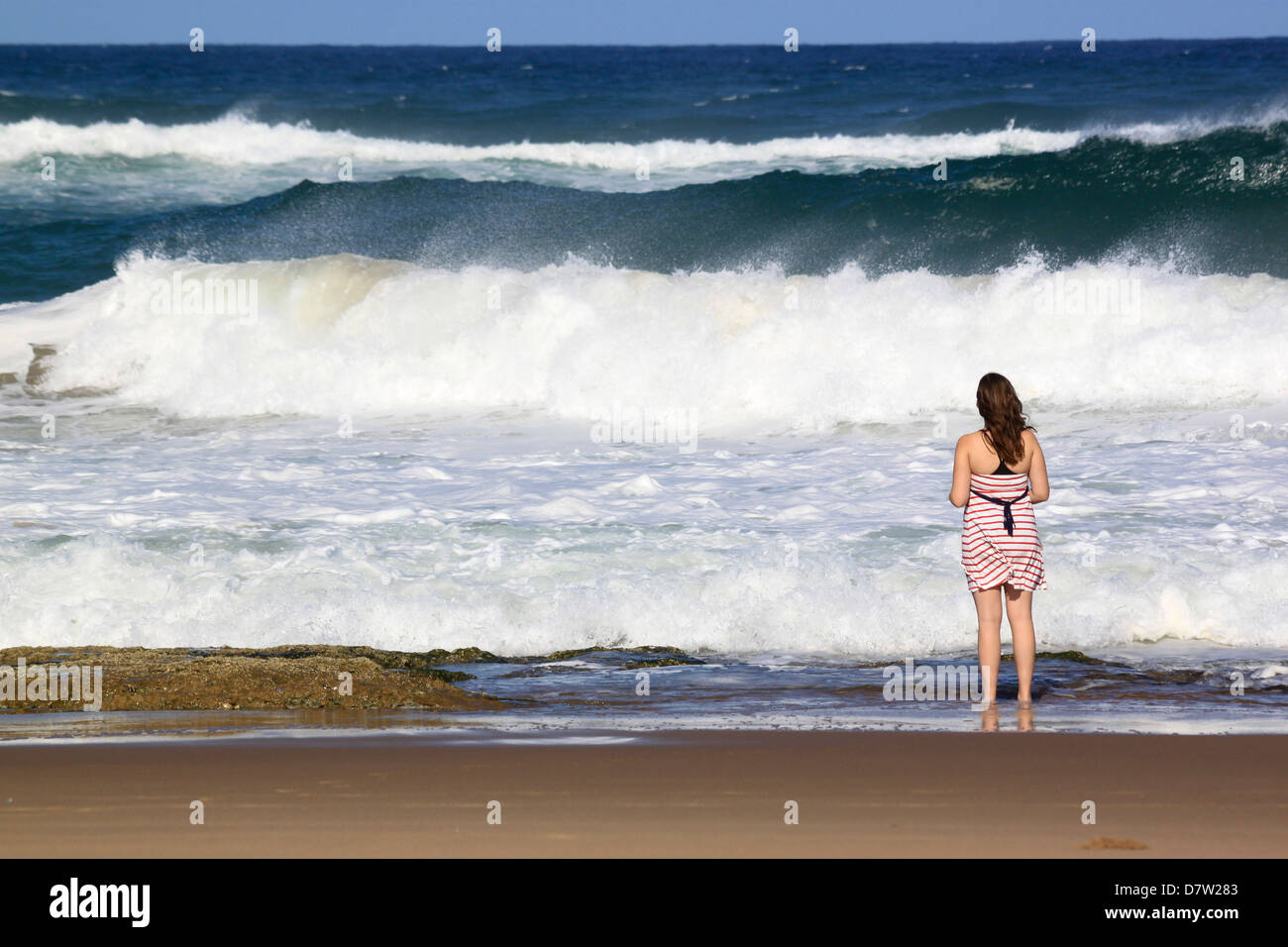 A young woman stands by crashing waves at the beach, St. Lucia Wetlands, Kwa-Zulu Natal, South Africa Stock Photo