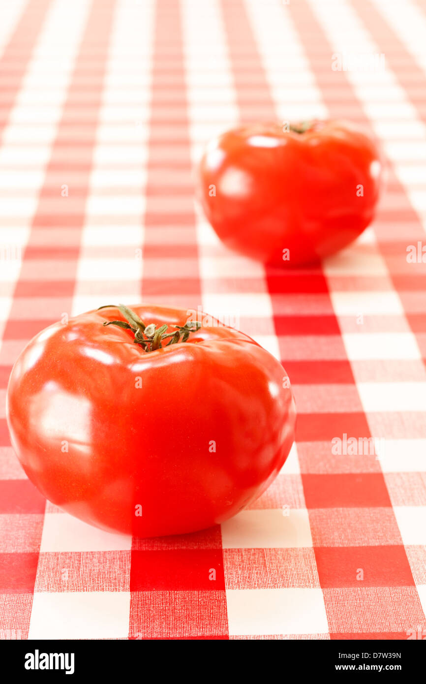 Two tomatoes on red tablecloth. Stock Photo