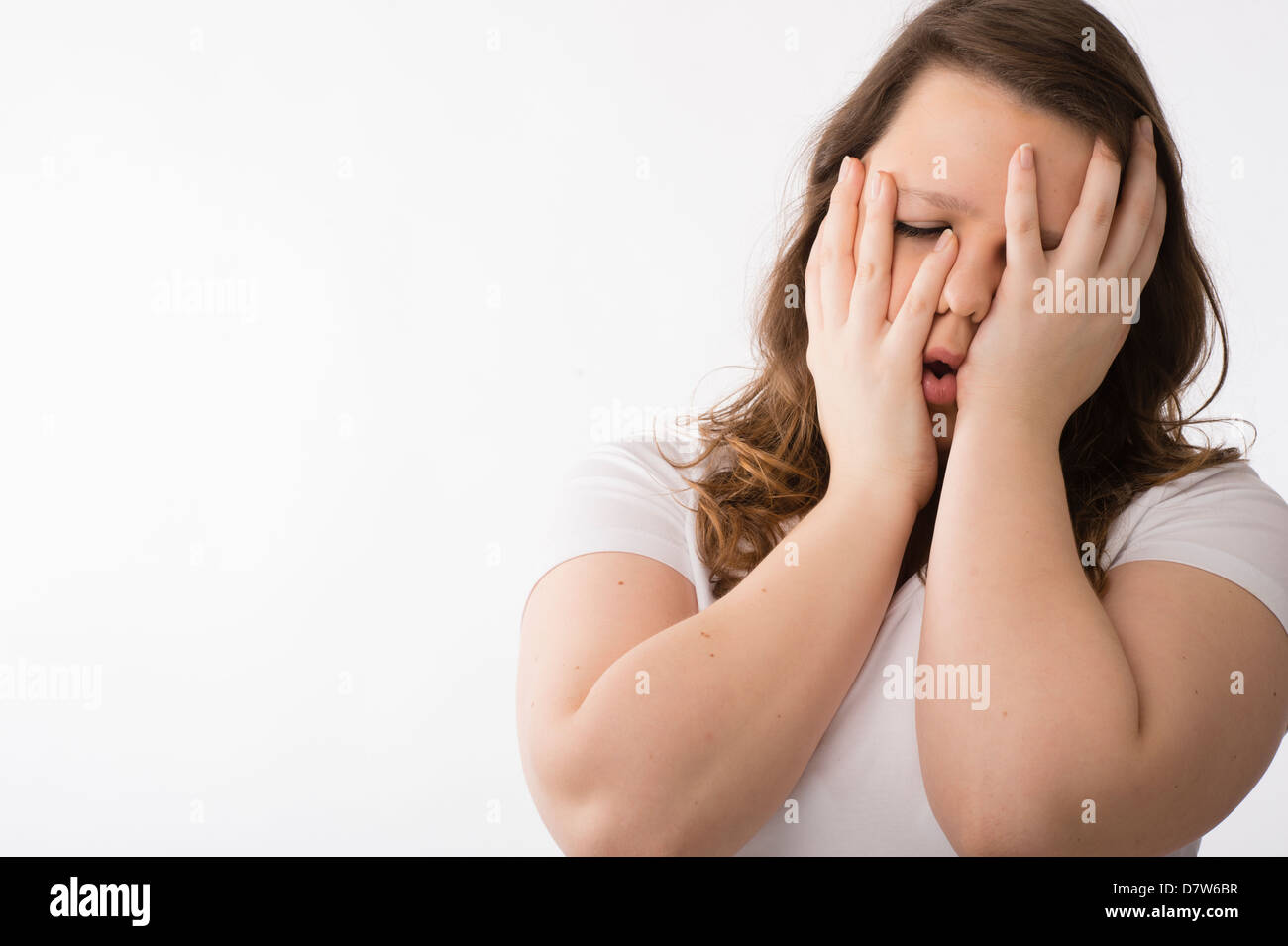 A young brunette teenage Caucasian girl ill sick hungover holding her face in her hands Stock Photo