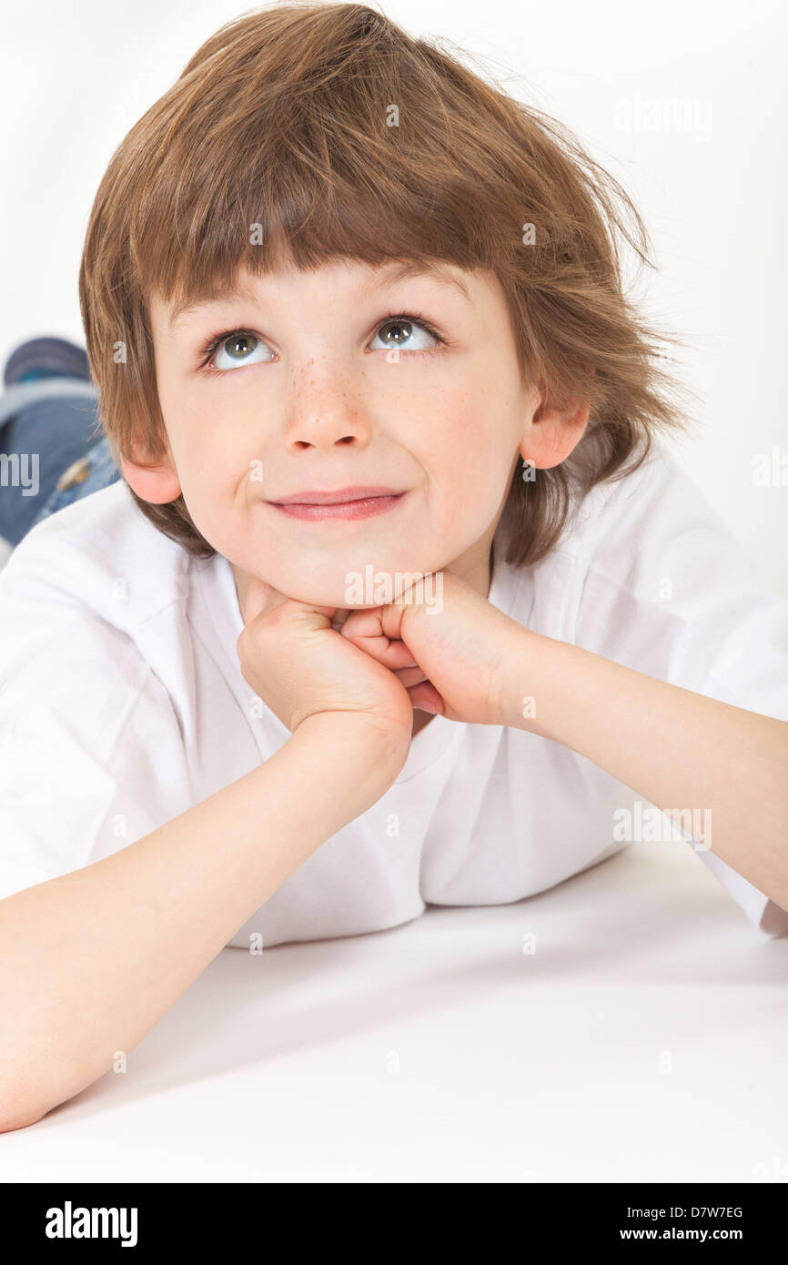 White background studio photograph of young happy boy child laying down, resting on hands