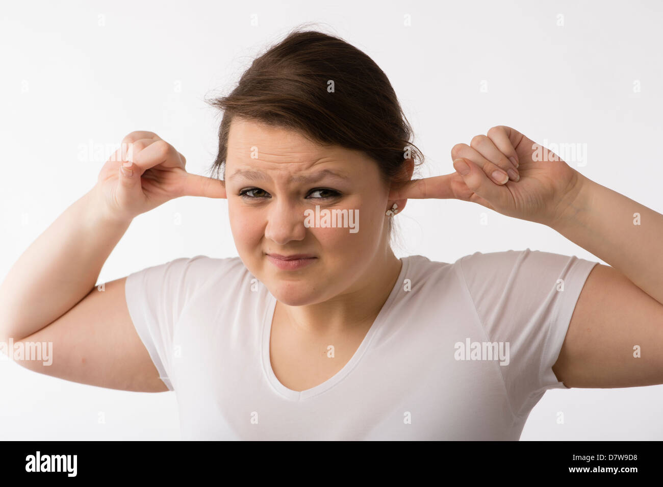 A young brunette teenage Caucasian girl with her fingers in her ears keeping out loud noise sounds Stock Photo