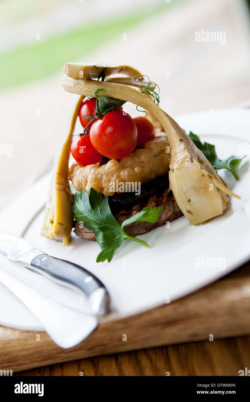 Sirloin steak meal served with artichoke, Onion rings and fresh vine tomatoes on a white plate with cutlery. Stock Photo