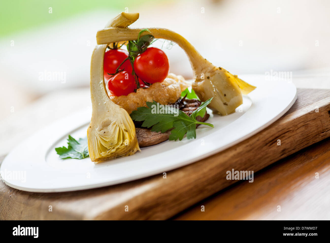 Sirloin steak meal served with artichoke, Onion rings and fresh vine tomatoes in a white plate on a wooden block Stock Photo