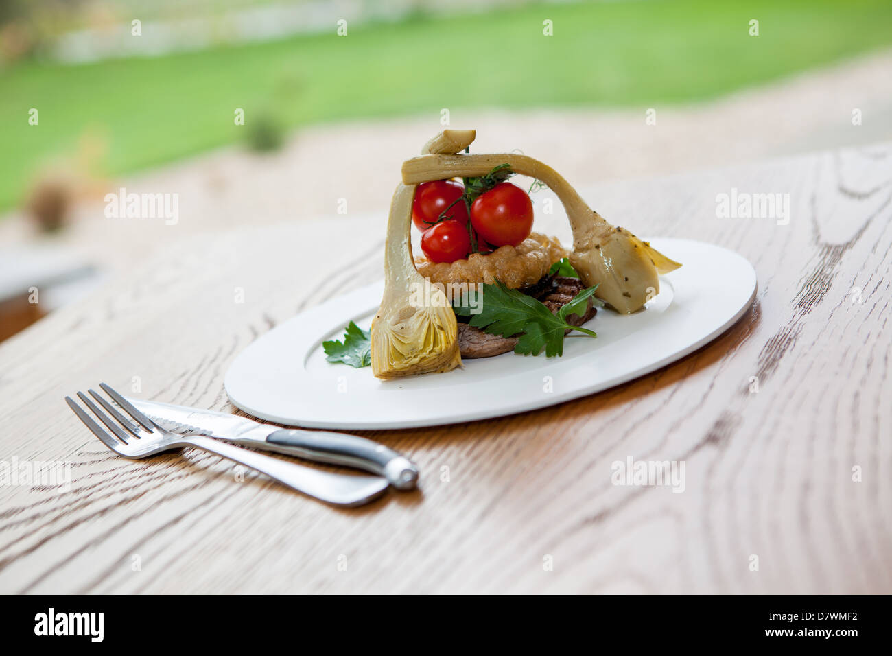 Sirloin steak meal served with artichoke, Onion rings and fresh vine tomatoes on a white plate with cutlery. Stock Photo