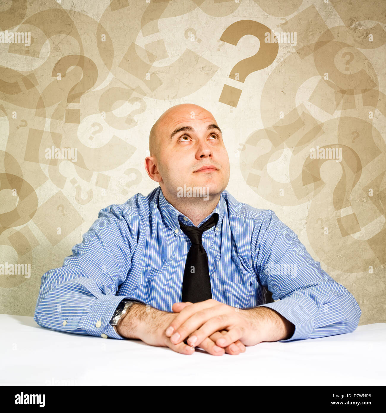 Businessman thinking and questioning, looking at question marks around his head. Stock Photo
