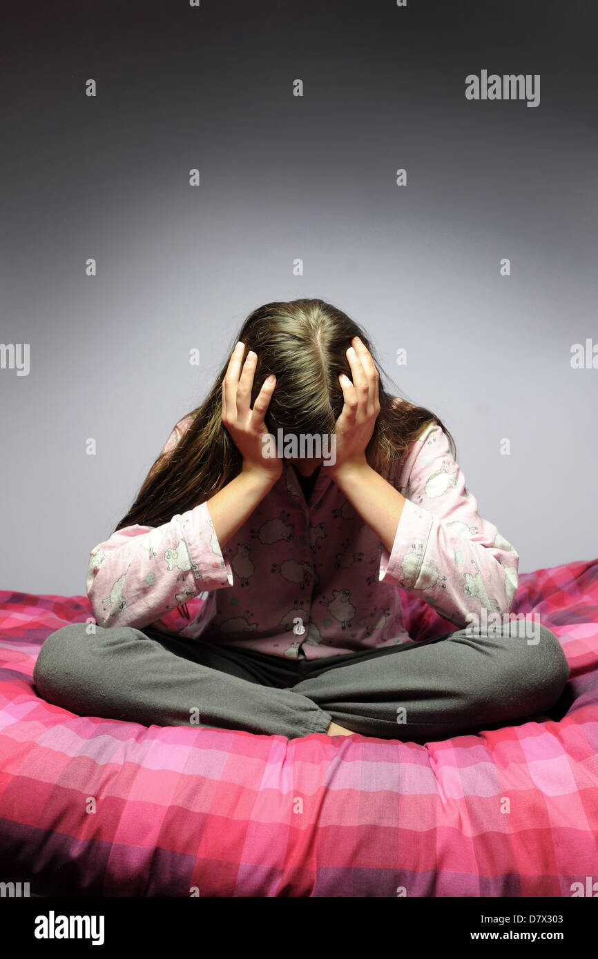 A depressed teenager sits in her bedroom with her head in her hands. Stock Photo