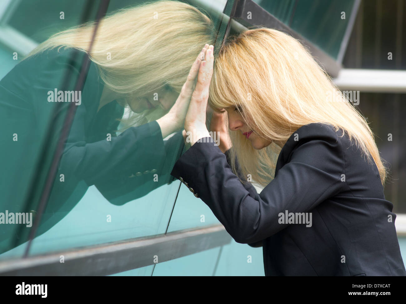 A depressed business woman takes a moment to herself leaning against the office window. Stock Photo