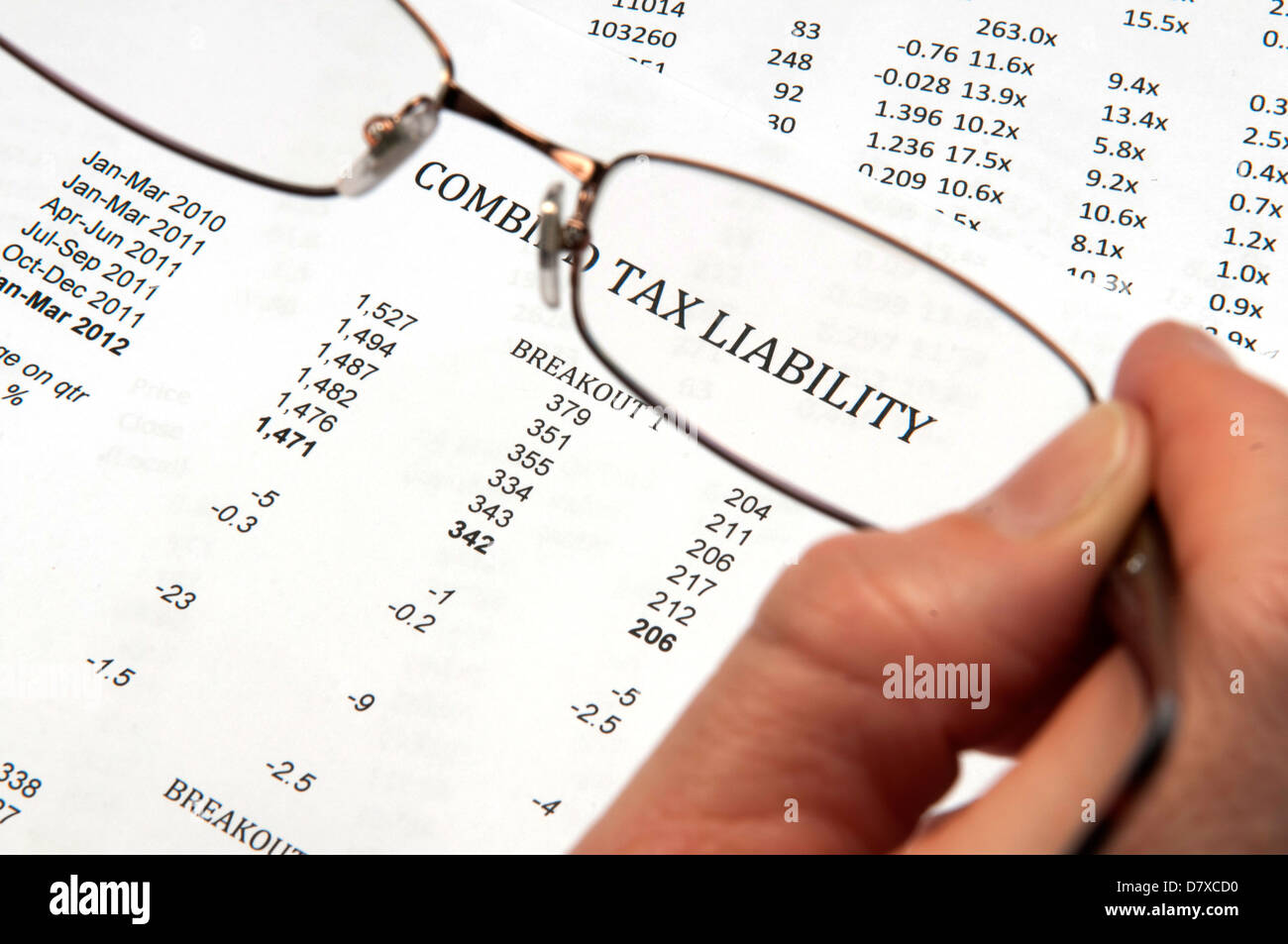 Hand holding magnifying glasses showing the words tax liability on financial paper Stock Photo