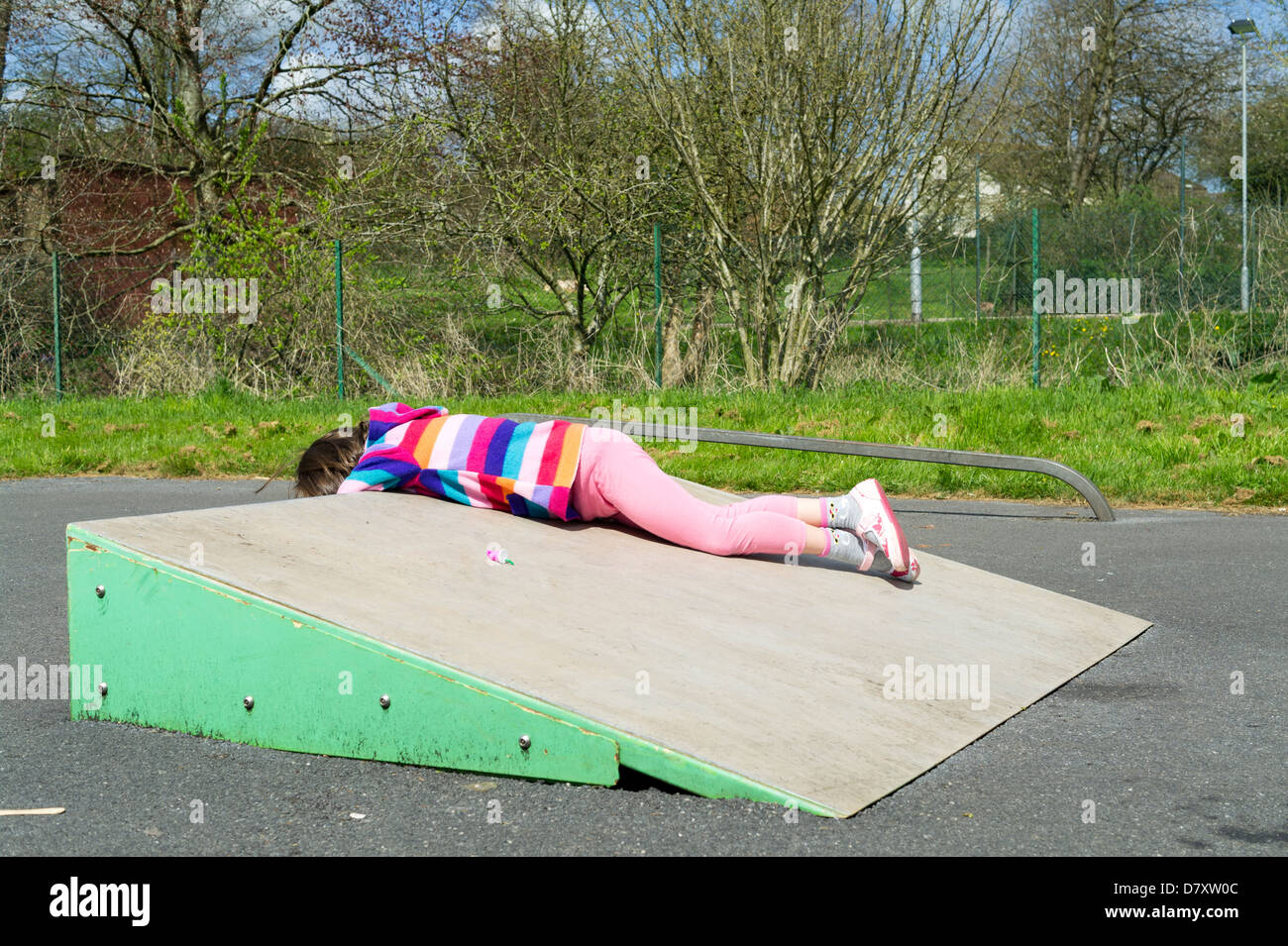 Six year old girl playing on skate ramp in a playground. Stock Photo