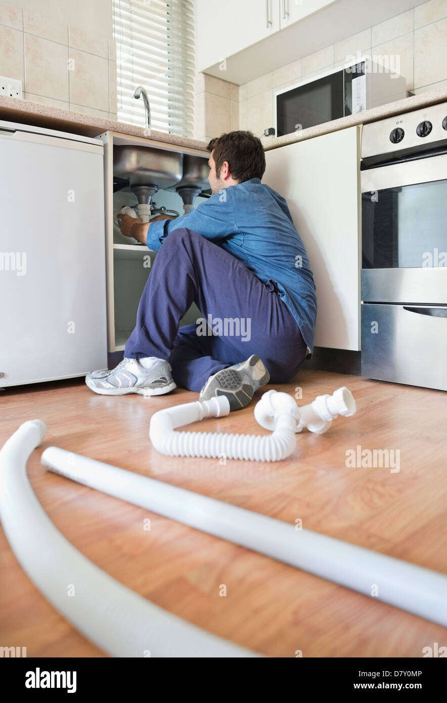 Plumber working on pipes under sink Stock Photo