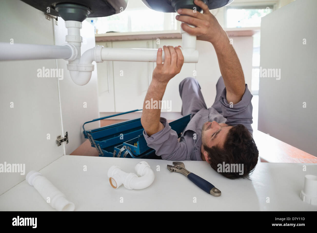 Plumber Working On Pipes Under Kitchen Sink Stock Photo