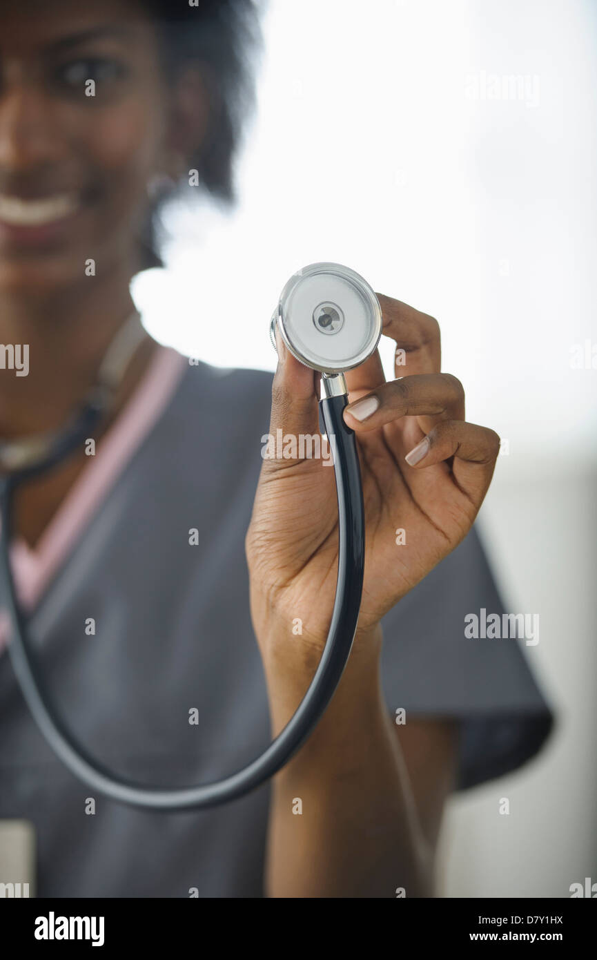 Black nurse holding up stethoscope Stock Photo